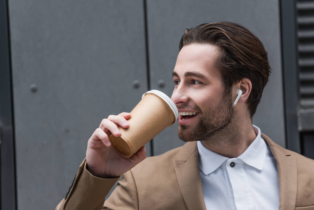 feliz hombre de negocios en los auriculares beber café para ir cerca de la construcción - Foto, imagen