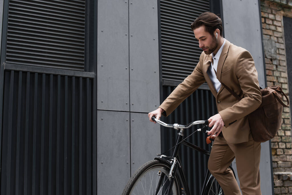 homem de negócios barbudo em fones de ouvido andar de bicicleta fora  - Foto, Imagem