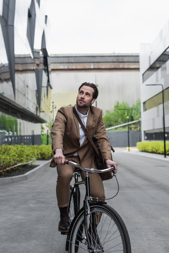 longitud completa de hombre de negocios en auriculares montar en bicicleta cerca de edificios - Foto, imagen