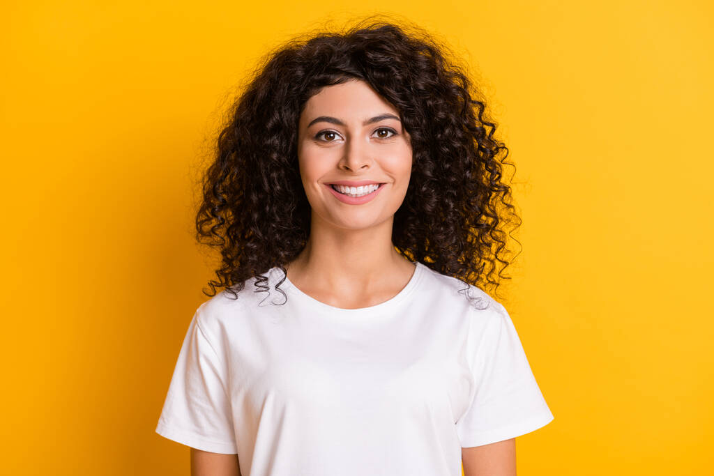 Фотопортрет веселой курчавой брюнетки в белой футболке, улыбающейся изолированно на ярко-желтом фоне - Фото, изображение
