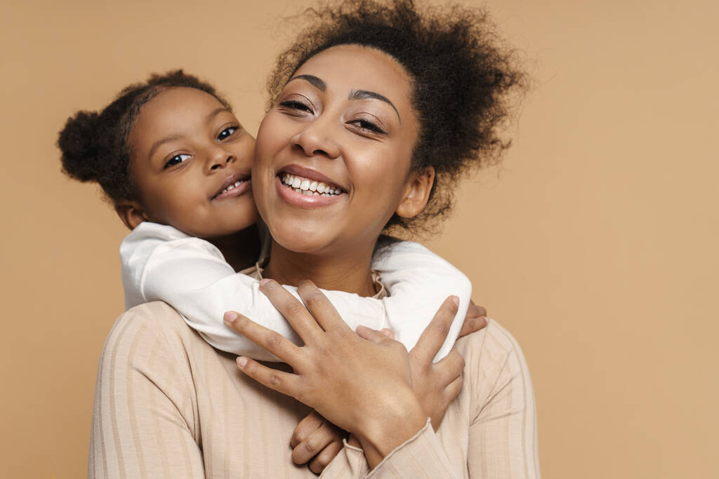 Χαρούμενη μαύρη μητέρα και κόρη αγκαλιασμένοι και χαμογελαστοί απομονωμένοι σε μπεζ φόντο - Φωτογραφία, εικόνα