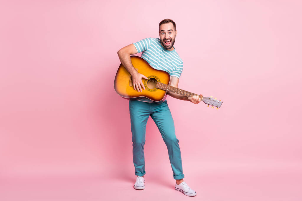 Размеры тела в полный рост вид симпатичного веселого парня, играющего на струнной гитаре в другом стиле, весело проводящего время на розовом фоне - Фото, изображение