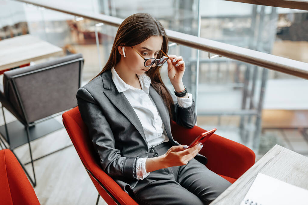 Бізнес-леді в окулярах на робочому місці використовує телефон і сидить за столом. Менеджер в офісі
. - Фото, зображення