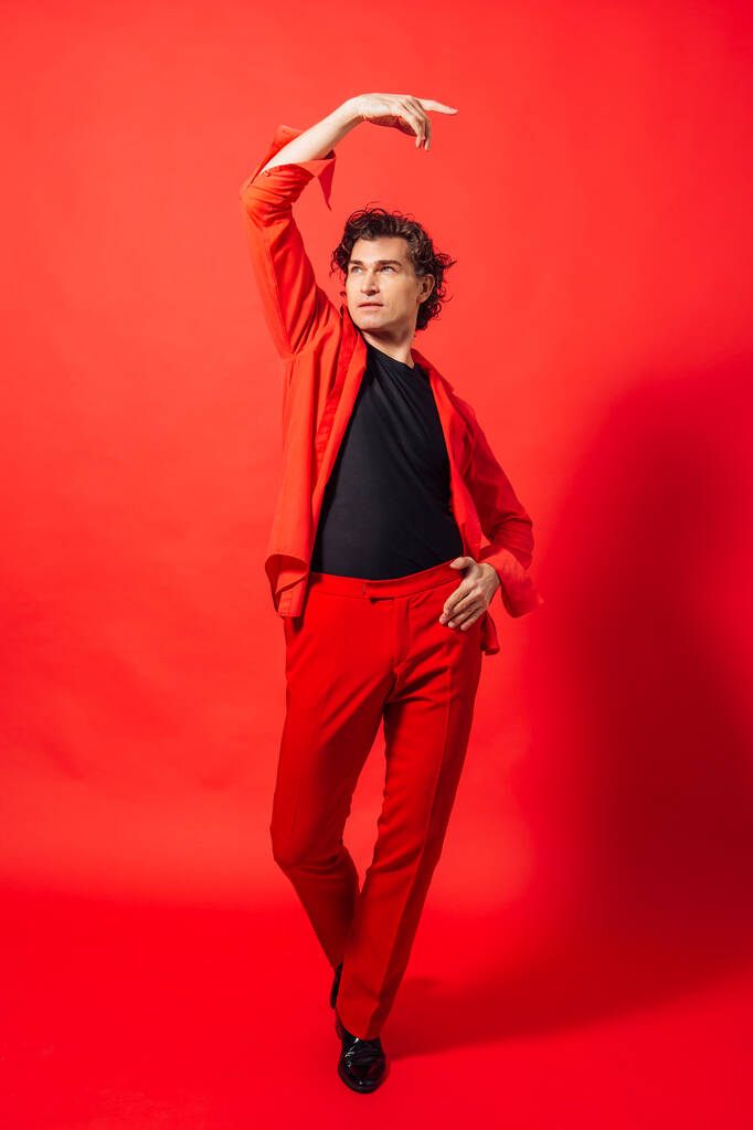 Πορτρέτο ενός ψηλού όμορφου άνδρα ντυμένου με κόκκινο πουκάμισο που ποζάρει στο κόκκινο φόντο. - Φωτογραφία, εικόνα