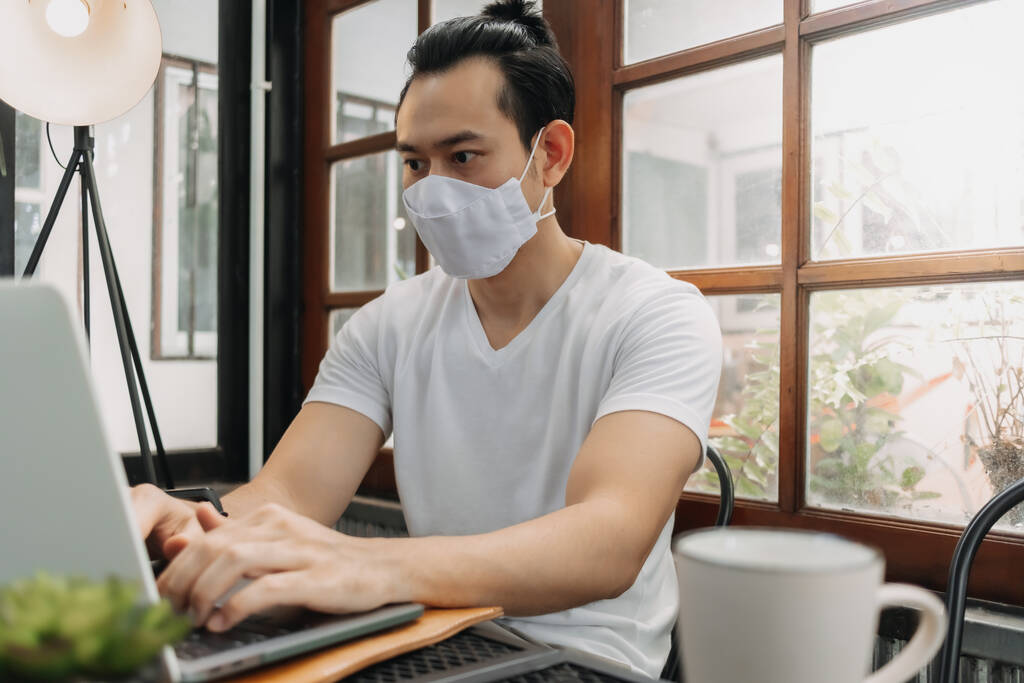 Mann trägt Maske bei der Arbeit mit Laptop im Café. - Foto, Bild