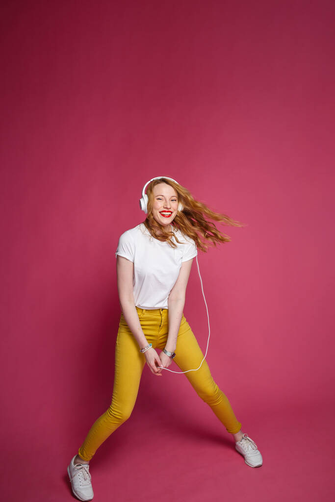 Atraktivní blondýna žena v bílých sluchátkách na růžovém pozadí - Fotografie, Obrázek