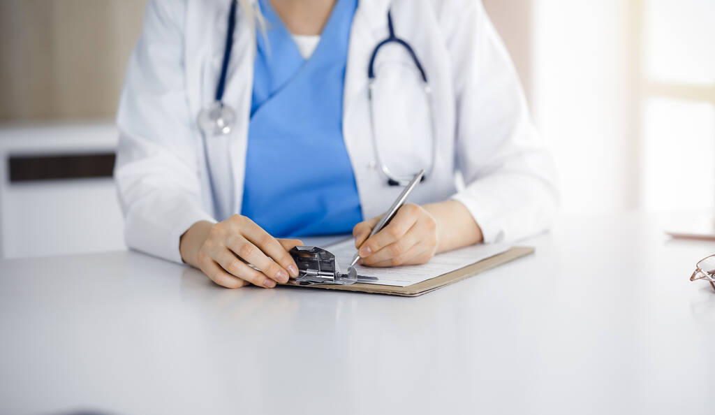 Onbekende vrouw-arts op het werk vullen medicatie geschiedenis record formulier in zonnige kliniek, close-up - Foto, afbeelding
