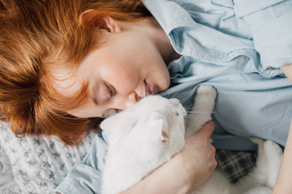 Kobieta obejmująca swojego ulubionego białego kota leżącego na łóżku - Zdjęcie, obraz
