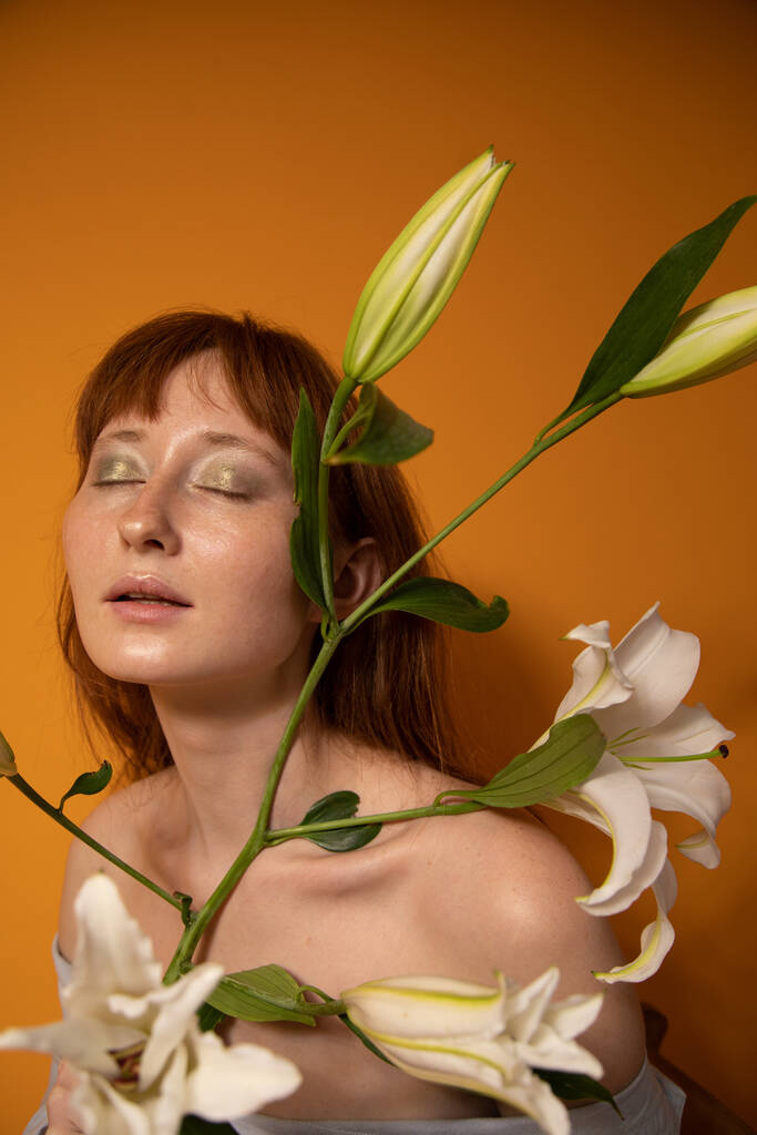 Kobieta z zielonymi oczkami zamknęła oczy i trzymała lilie podczas pozowania - Zdjęcie, obraz