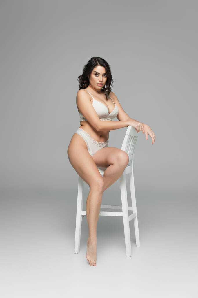 Sexy vrouw in lingerie zitten op stoel op grijze achtergrond  - Foto, afbeelding
