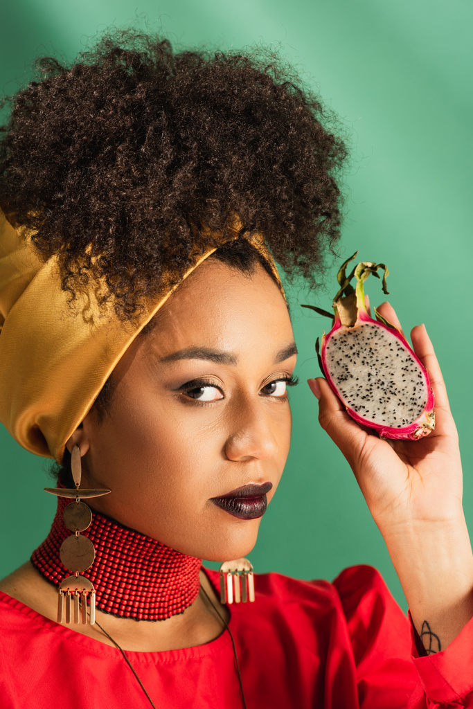 young african american woman holding half cut of dragon fruit on green - Photo, Image