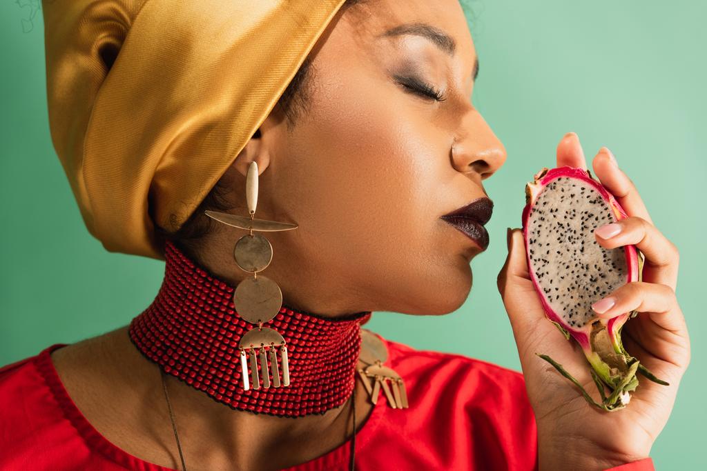 young african american woman with closed eyes holding half cut of dragon fruit on green - Photo, Image