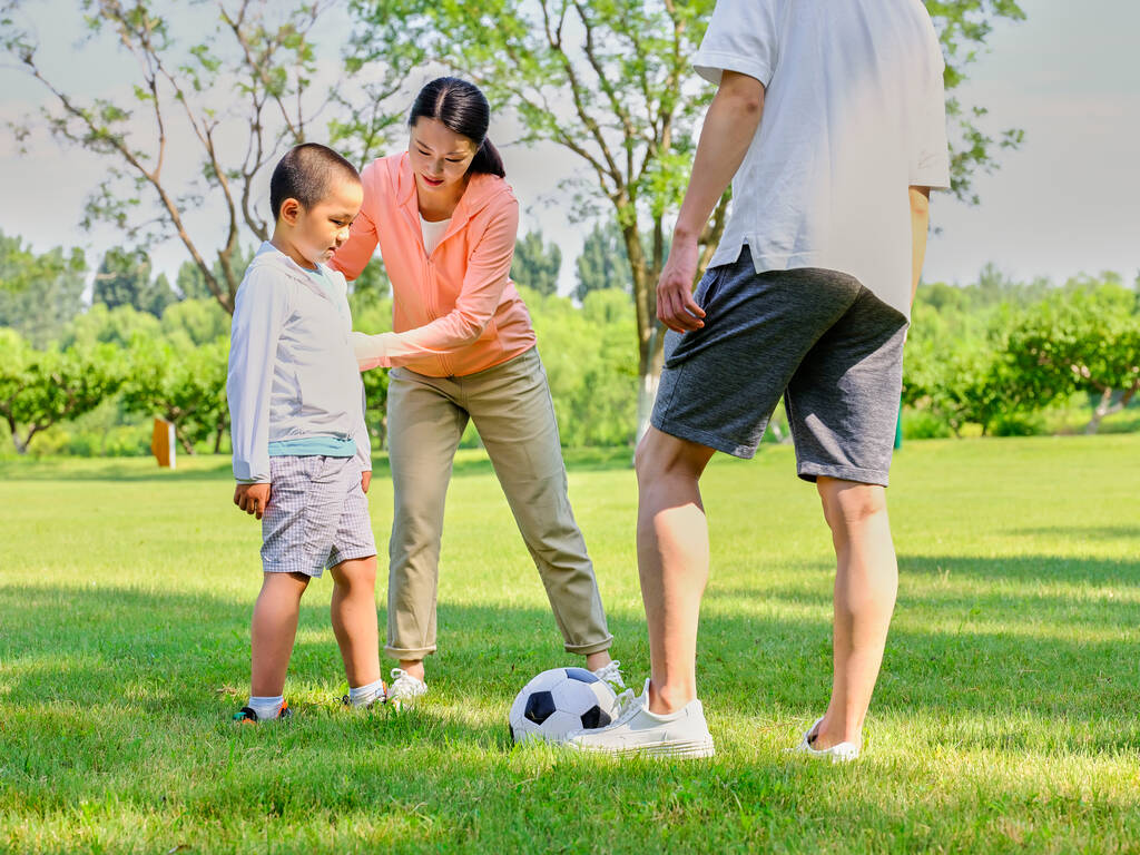 Счастливая семья из трех человек играет в футбол в парке - Фото, изображение