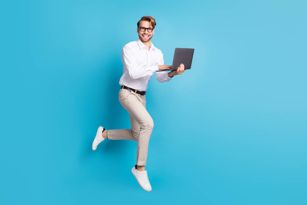 Full length body size view of attractive cheerful man jumping using laptop it expert isolated over bright blue color background - Photo, Image