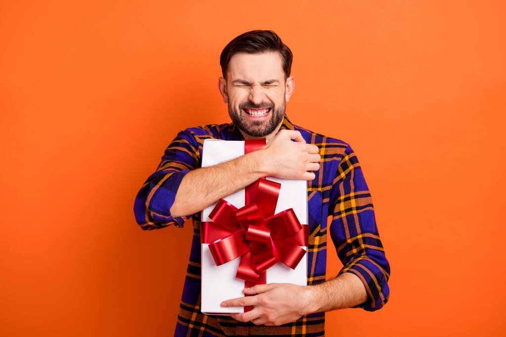 Фото веселого человека с закрытыми глазами зубастые улыбки руки держат обнимашки Giftbox изолированы на оранжевом фоне цвета - Фото, изображение