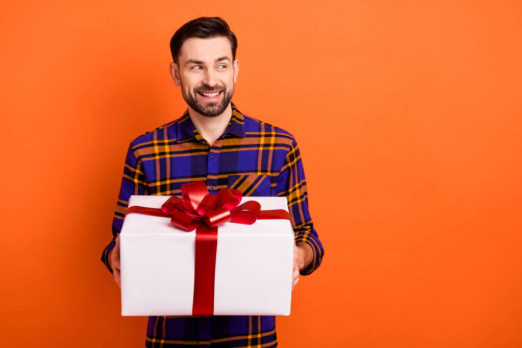 Portrait de la personne satisfaite bras tenir boîte cadeau regard intéressé espace vide isolé sur fond de couleur orange - Photo, image