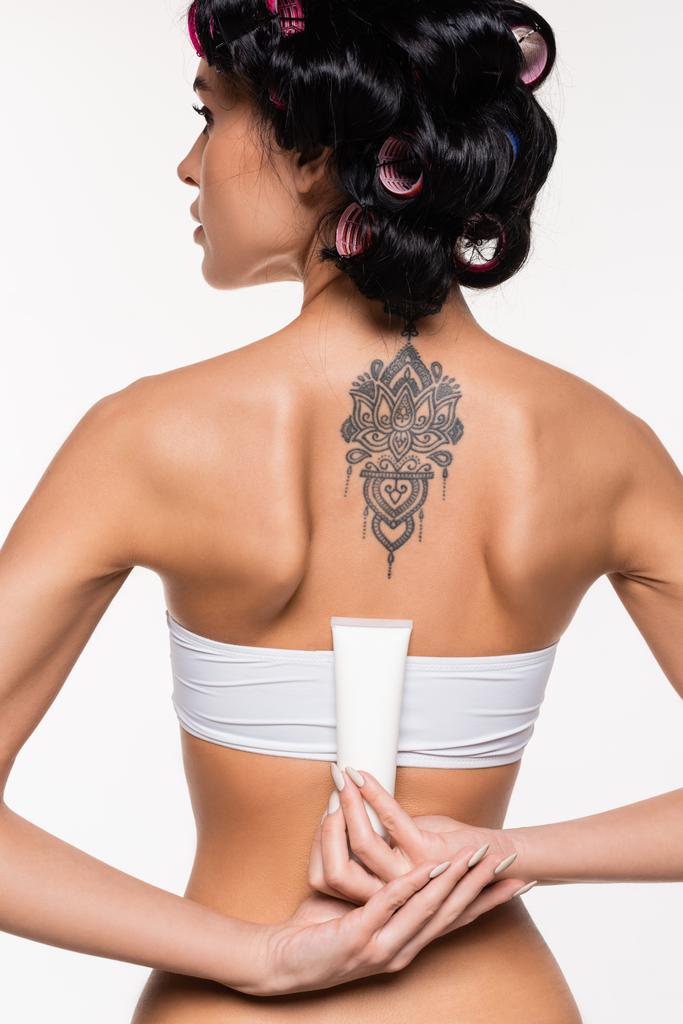 back view of young woman in curlers with tattoo on back holding cream tube isolated on white - Φωτογραφία, εικόνα