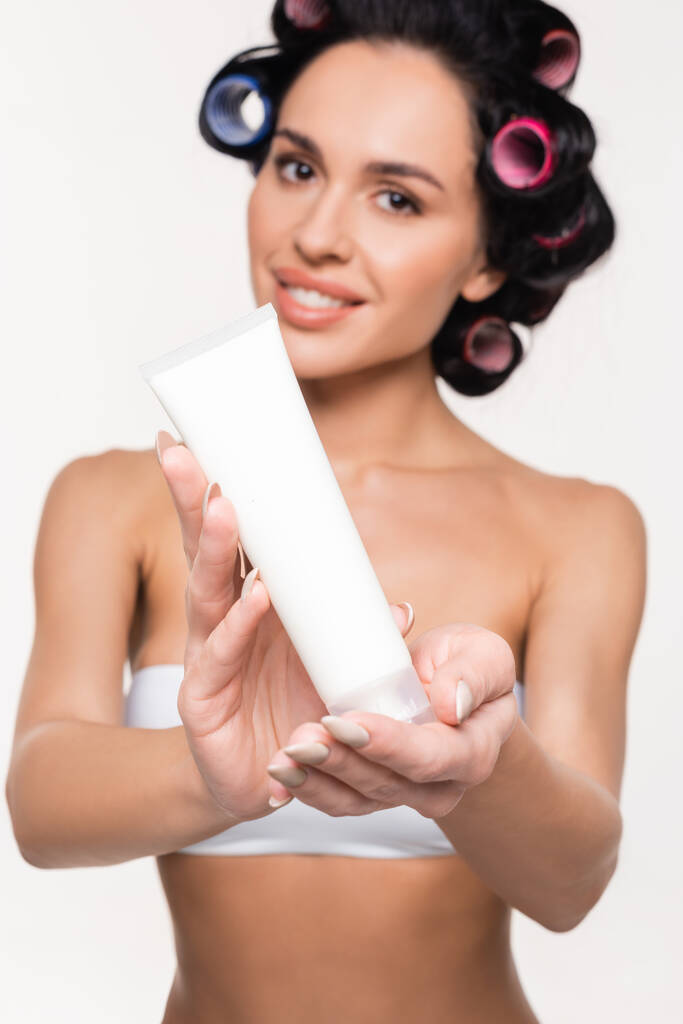 crema tubo in mani di sfocato sorridente giovane donna in bigodini isolato su bianco - Foto, immagini