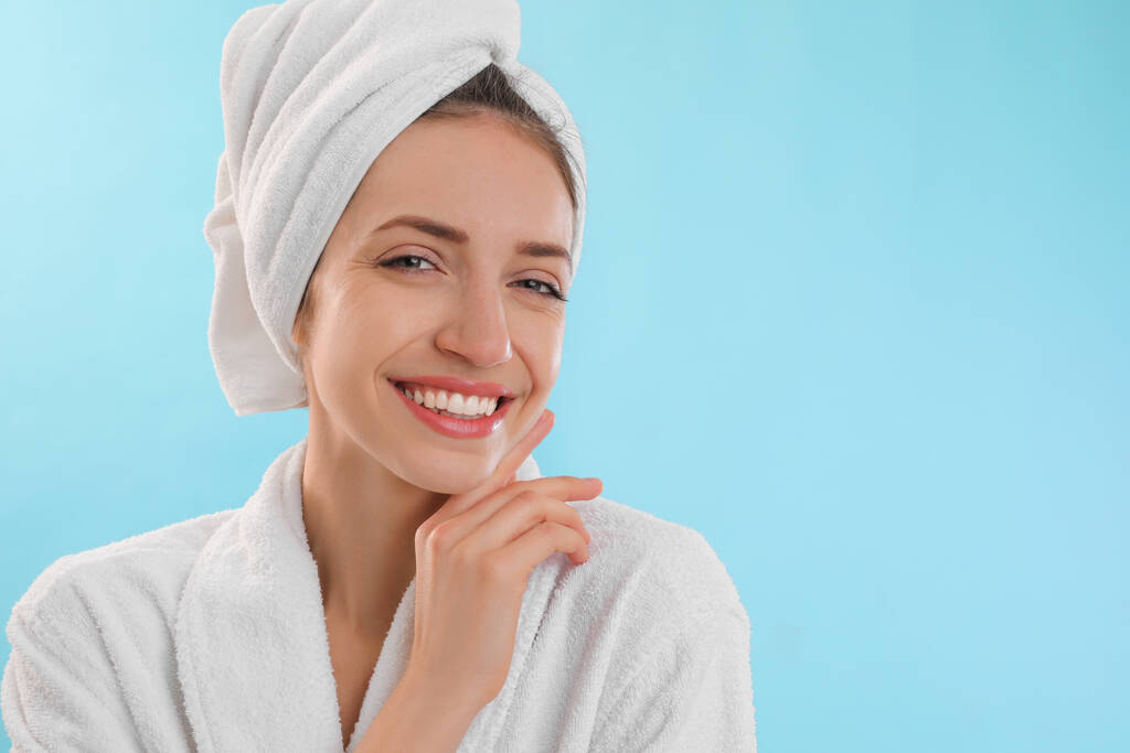 Mooie jonge vrouw met haar gewikkeld in handdoek na het wassen op lichtblauwe achtergrond. Ruimte voor tekst - Foto, afbeelding