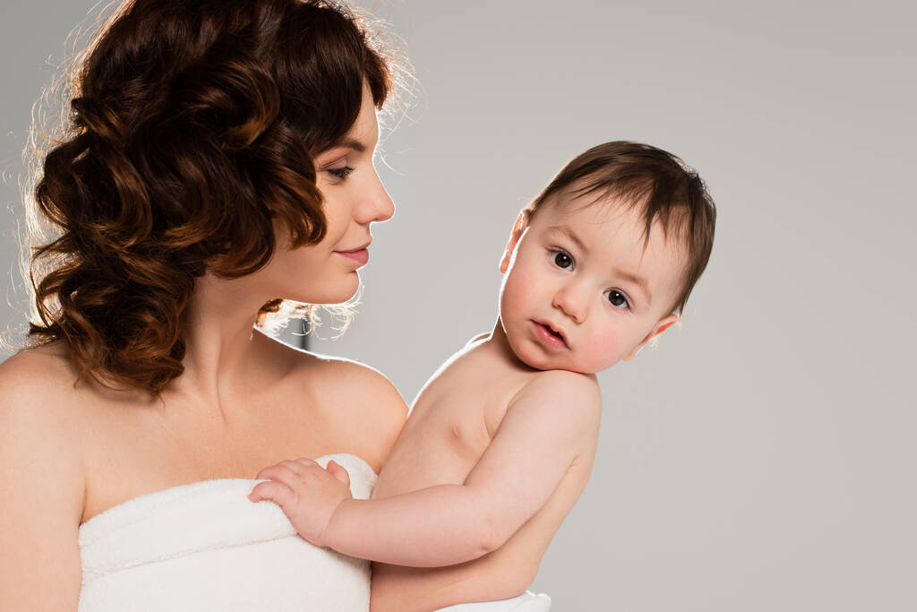 кучерява мати з голими плечима тримає маленького сина в руках ізольовано на сірому
  - Фото, зображення