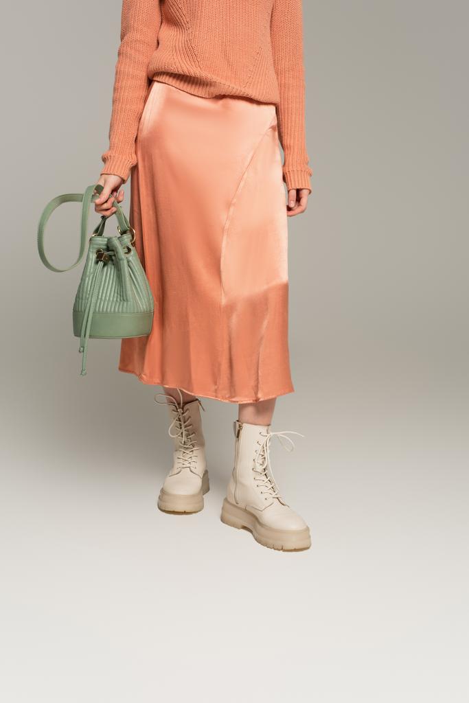 bijgesneden weergave van trendy vrouw in satijnen rok holding bag op grijs - Foto, afbeelding