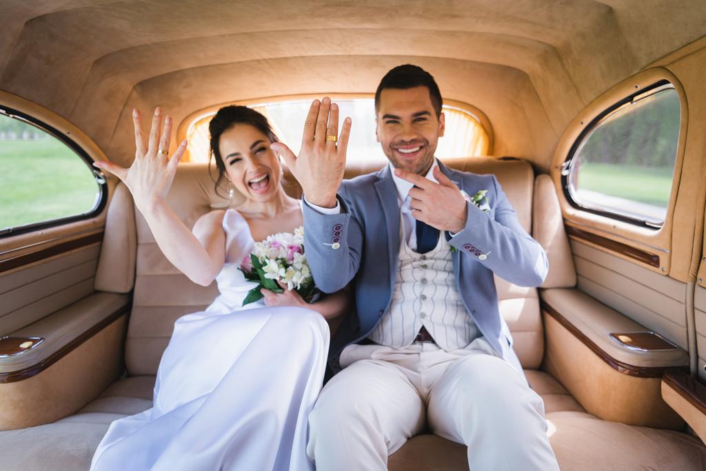 Nouveaux mariés flous montrant des anneaux dans la voiture rétro  - Photo, image