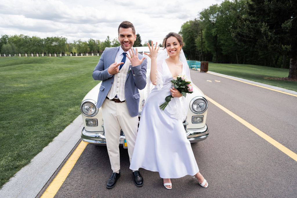 Vidám friss házasok gyűrűk közelében retro auto az úton - Fotó, kép