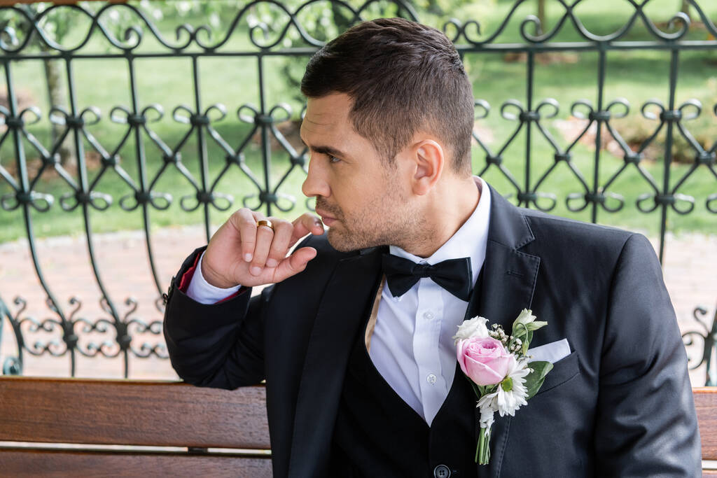 Vista laterale dello sposo con boutonniere sulla giacca distogliendo lo sguardo sulla panca  - Foto, immagini