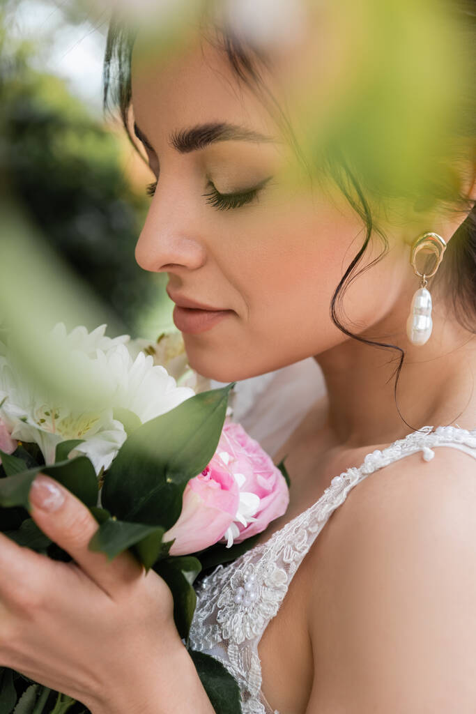 Seitenansicht der jungen Braut mit Blumenstrauß auf verschwommenem Vordergrund  - Foto, Bild
