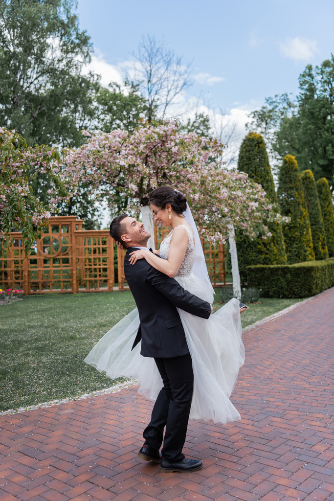 Πλευρική άποψη του χαμογελαστού γαμπρού κρατώντας στα χέρια όμορφη νύφη στο πάρκο  - Φωτογραφία, εικόνα