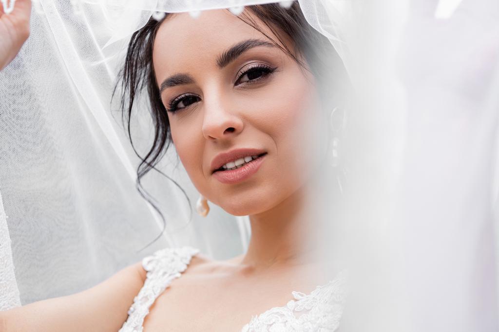 Mladá nevěsta ve svatebních šatech drží rozmazaný závoj  - Fotografie, Obrázek