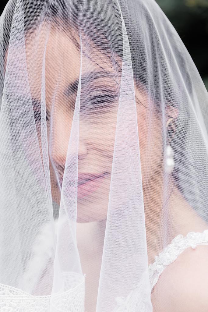 Csinos menyasszony fehér fátyolban a kamerába néz  - Fotó, kép