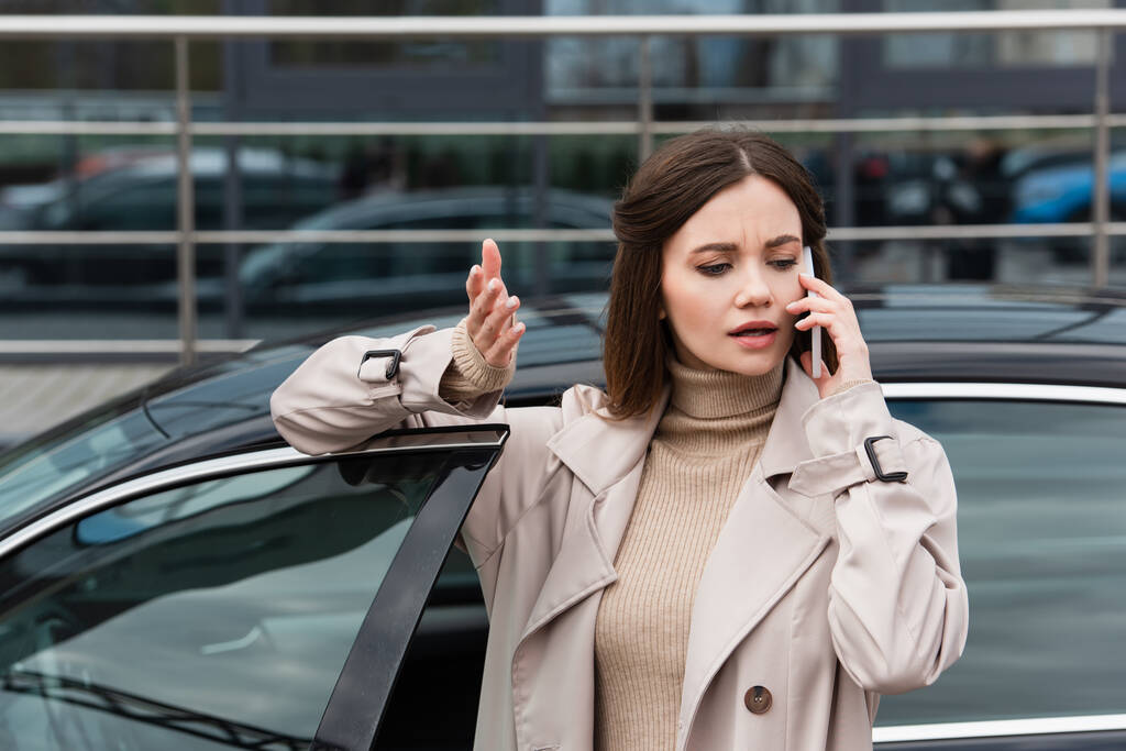 young woman gesturing while talking on cellphone near car - Photo, Image