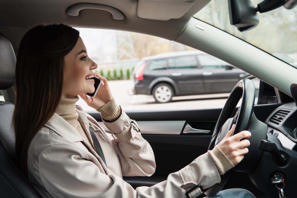 боковой вид довольной женщины, разговаривающей по мобильному телефону за рулем автомобиля - Фото, изображение