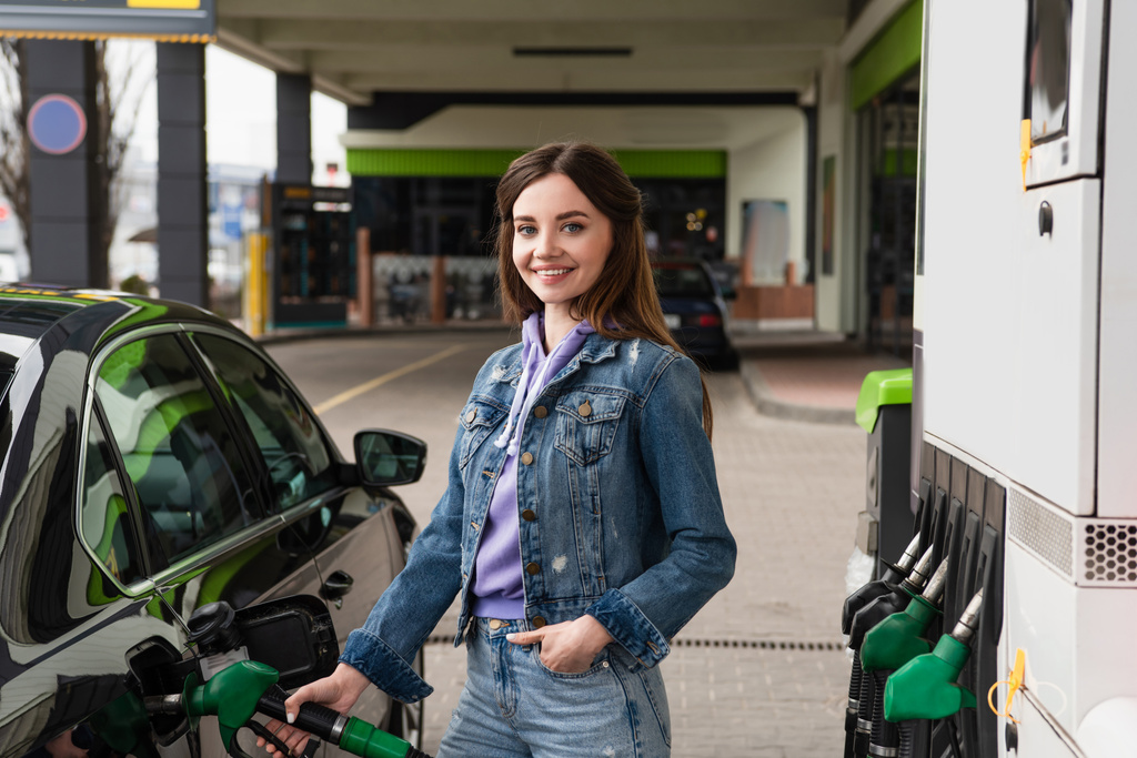 ガソリンスタンドで車を補充するジーンズのポケットに手できれいな女性 - 写真・画像