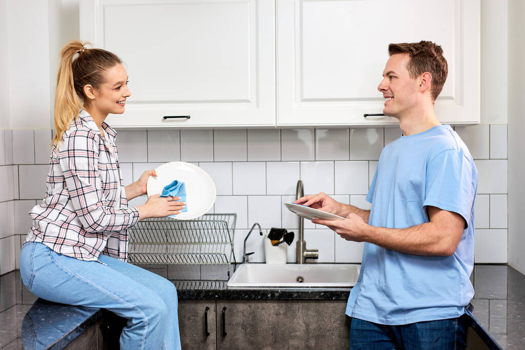 Alegre pareja caucásica lavando platos juntos en el interior, manteniendo la casa ordenada - Foto, imagen