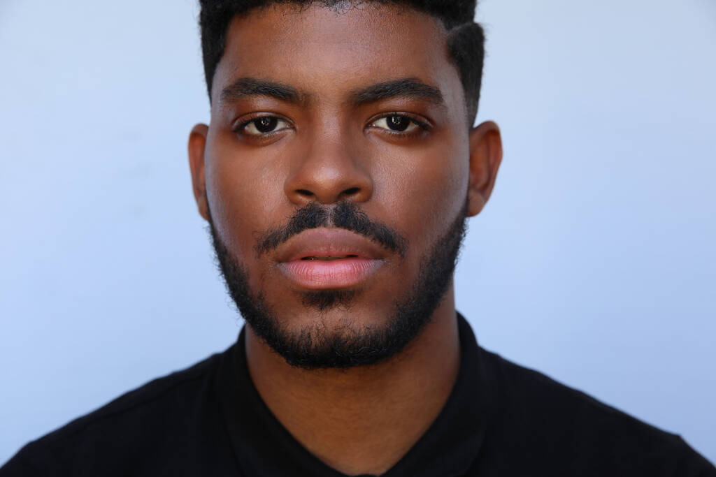 Καλλιεργημένη εικόνα ενός όμορφου νεαρού μαύρου άνδρα που κοιτάζει μια πλευρά σε λευκό φόντο. - Φωτογραφία, εικόνα