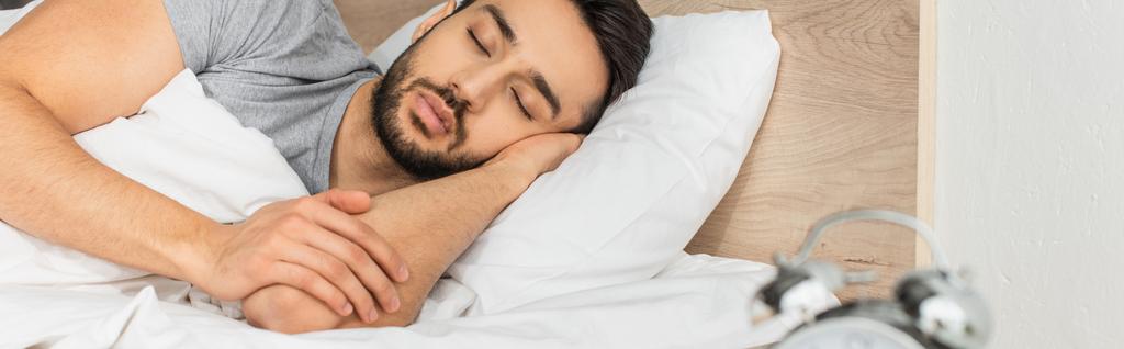 Reloj despertador borroso cerca del hombre dormido en casa, pancarta  - Foto, imagen