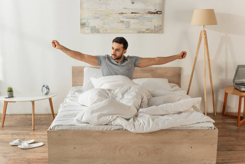 uomo barbuto stretching mentre seduto sul letto al mattino  - Foto, immagini