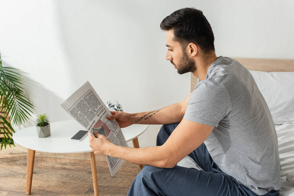 Seitenansicht eines Mannes im Pyjama, der Zeitung auf dem Bett liest  - Foto, Bild