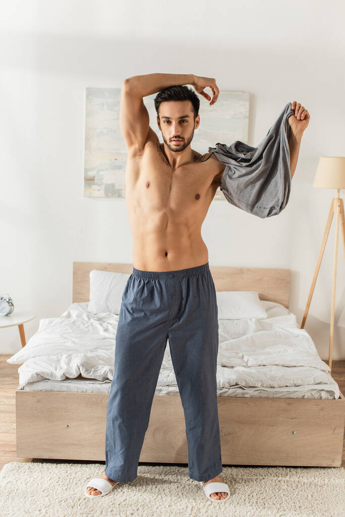 Bärtiger Mann zieht T-Shirt im Schlafzimmer aus  - Foto, Bild