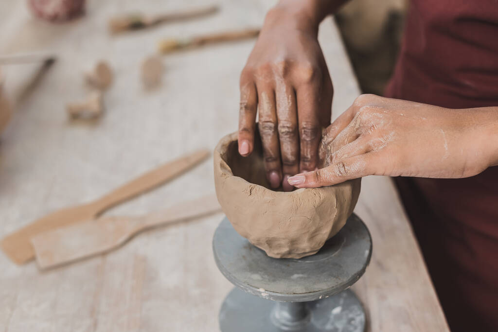 vista parcial de la joven afroamericana esculpiendo olla de barro con manos en cerámica - Foto, Imagen