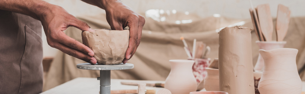 vue partielle du jeune homme afro-américain sculptant pot d'argile avec les mains sur la table avec des équipements en poterie, bannière - Photo, image