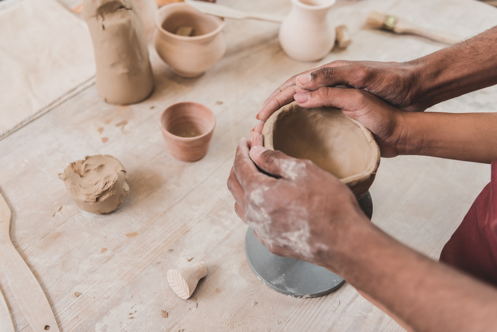 partial view of young african american couple sculpting clay pot with holding hands together in pottery - Photo, Image