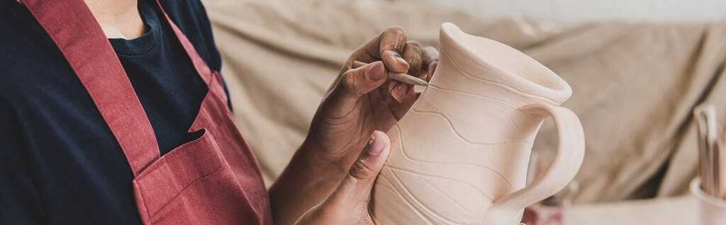 vista parziale di giovane donna afroamericana che scolpisce vaso di argilla con bastone in ceramica, striscione - Foto, immagini