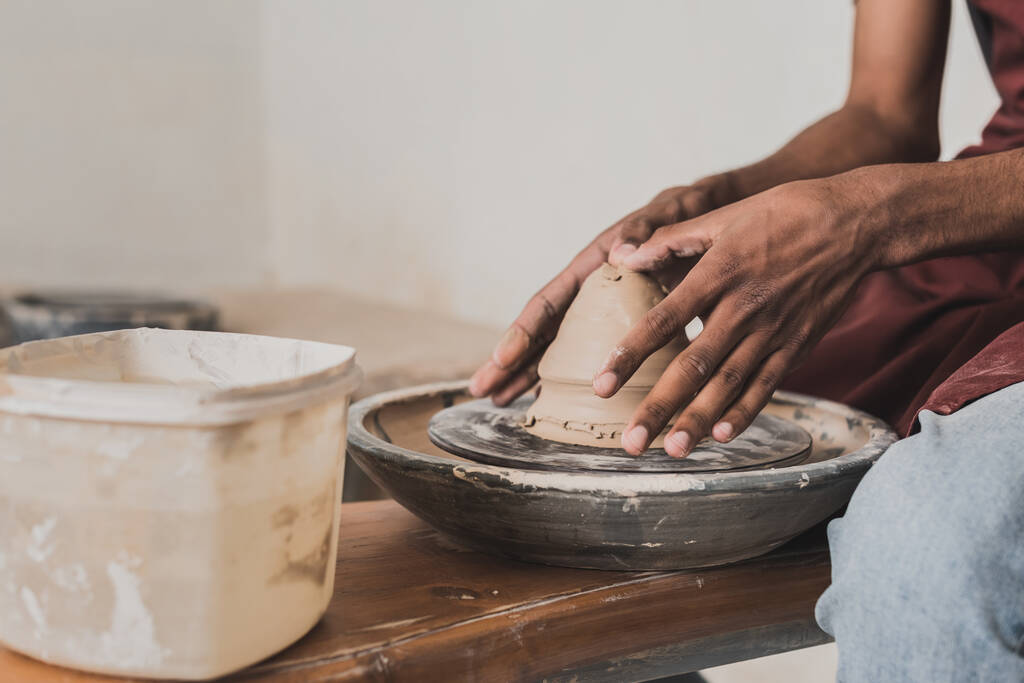 visão parcial do jovem afro-americano modelando argila molhada na roda em cerâmica - Foto, Imagem