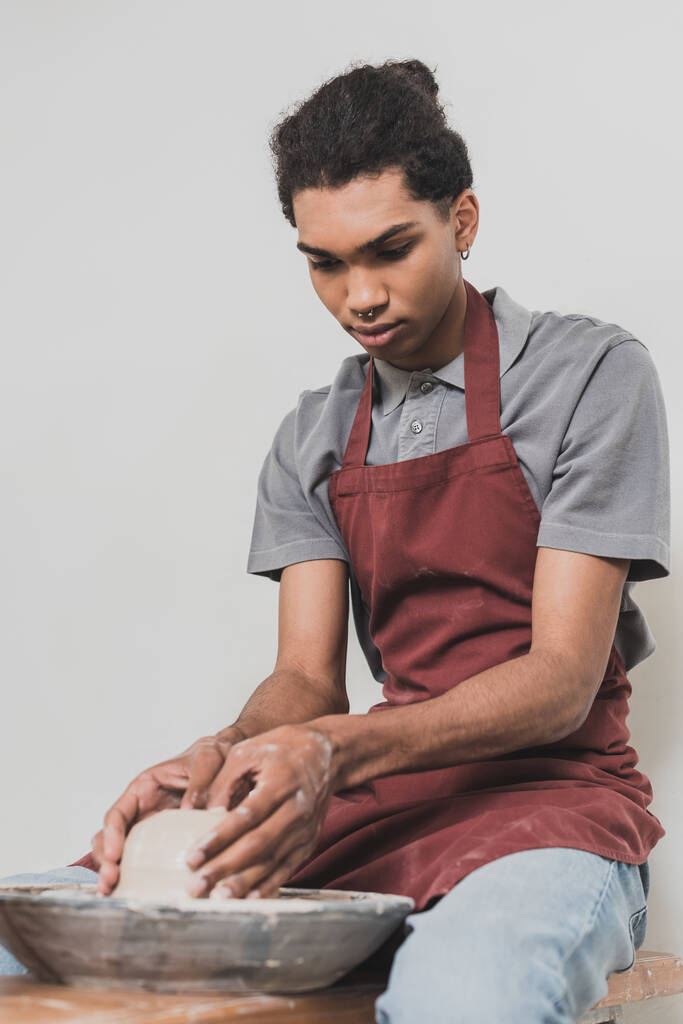serieus jong Afrikaans amerikaanse man modelleren natte klei op wiel met handen in aardewerk - Foto, afbeelding