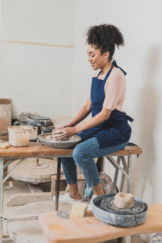sorridente giovane donna afro-americana che modella argilla bagnata su ruota con le mani in ceramica - Foto, immagini