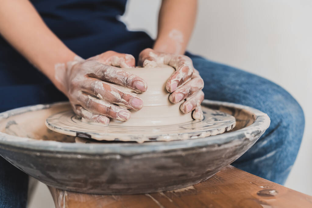 частичный вид молодой африканской женщины-американки, моделирующей мокрую глину на колесах с руками в керамике - Фото, изображение