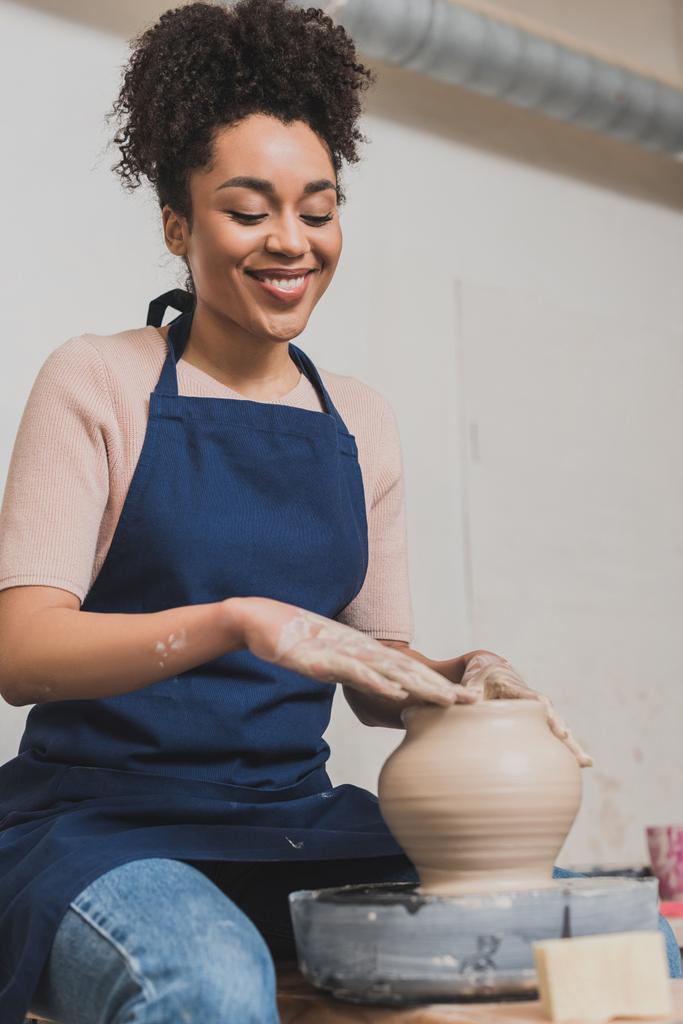 smiling young african american woman shaping wet clay pot on wheel in pottery - Fotoğraf, Görsel